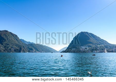 Panoramic landscape view of beautiful serene blue Gulf of Lugano lake and the mountain San Salvatore against clear blue sky and hills in Lugano Canton of Ticino Switzerland