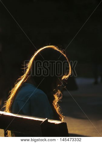 A girl sitting on the bench against the backdrop of the setting sun