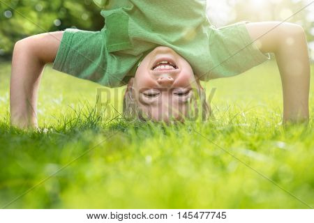 Young boy doing a headstand on the grass in the summer sunshine