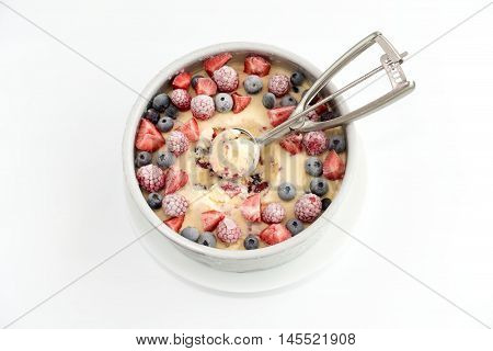 Homemade cheesecake ice cream with berries decorated with blueberries strawberries and raspberries in a round baking form. Ice cream scoop on top of ice cream. On white background.