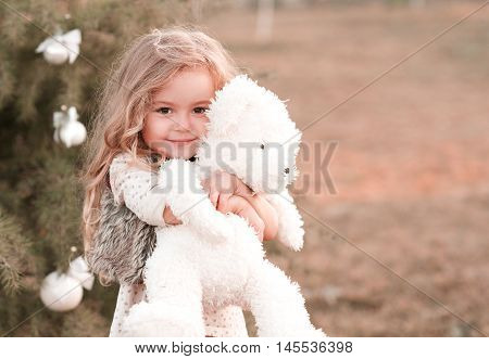 Smiling baby girl 4-5 year old holding teddy bear outdoors. Looking at camera. Childhood. Playful. Wearing stylish clothes.