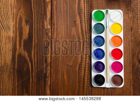 The palette of watercolor paints on a wooden background. Copy space