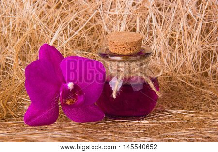 Spa composition on natural mat. Small bottle and pink orchid. Sizal