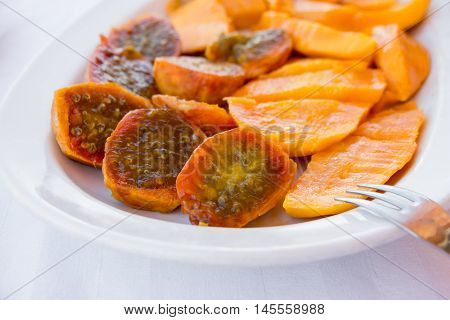 Prickly pear cactus fruits and mango fruits cutted in pieces on the white plate and background. Salad of mango and prickly pear cactus fruits in a white plate. Horizontal. Close.
