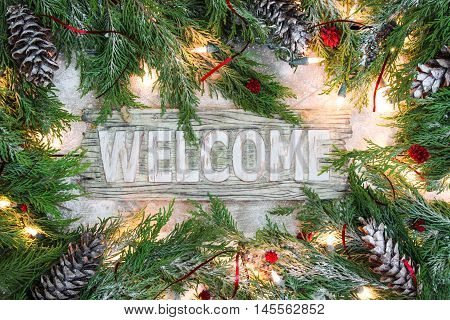 Holiday welcome sign with  green Christmas tree garland border, snow and lights on antique rustic wooden background
