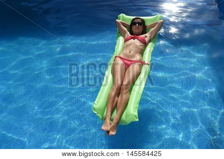 young happy beautiful woman in bikini and sunglasses lying relax on float airbed at vacation hotel resort swimming pool in Summer enjoying holidays having sunbath with tan body