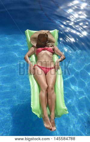 young beautiful woman in bikini and sun hat on face lying relax on float airbed at vacation hotel resort swimming pool in Summer enjoying holidays having sunbath with tan body