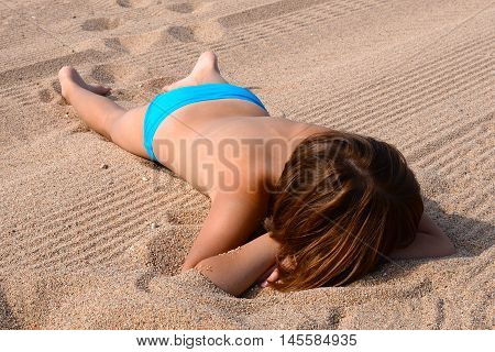 The girl sunbathes on the beach lying on the sand