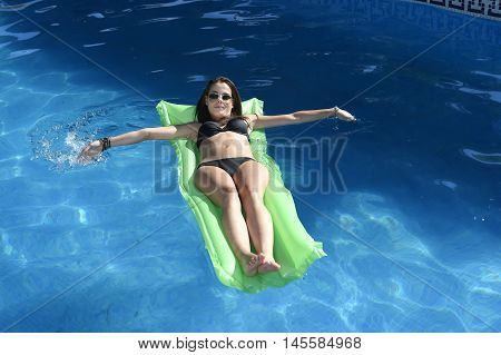 young happy beautiful woman in bikini and sunglasses lying relax on float airbed at vacation hotel resort swimming pool in Summer enjoying holidays having sunbath with tan body