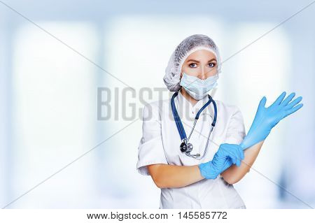 Medical surgeon doctor woman over blue clinic background. Doctor putting on sterile gloves. Place for medical advertise, medical advertising concept.