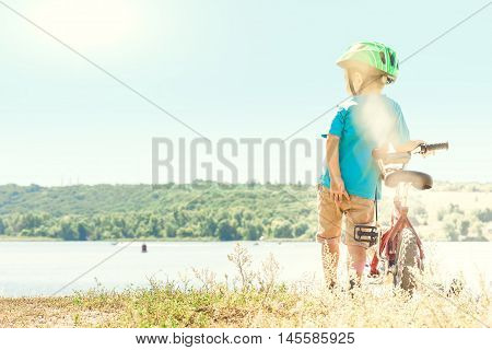 Kid helmet bicycle . Sun shines brightly. Child riding a bicycle. Child with a bicycle on the river bank. Beautiful baby. Toned image.