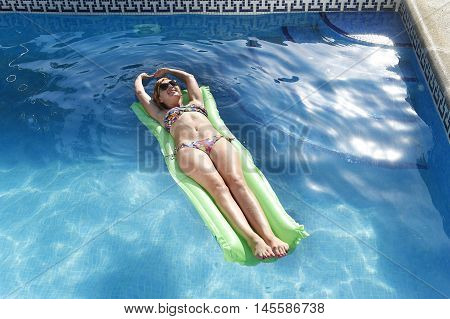 young happy beautiful woman in bikini and sunglasses lying relax on float airbed at vacation hotel resort swimming pool in Summer enjoying holidays having sunbath with tan body
