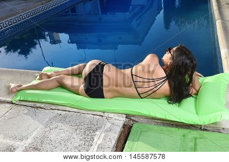 young sexy woman in bikini and sunglasses with fit beautiful body having suntan relaxing on airbed at swimming pool of vacation hotel resort in summer enjoying holidays
