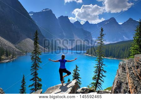 Woman in yoga pose meditating at Moraine Lake in Rocky Mountains. Banff National Park Alberta Canada.
