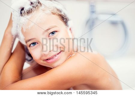 Cute young girl in shower washing hair and face with shampoo.