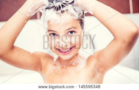 Cute young girl in shower washing hair and face with shampoo.