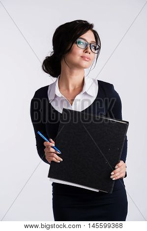 Young Caucasian woman wearing a dark blue dresst and and a white shirt, holding a ring binder folder and pen. Isolated on light background