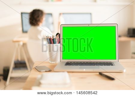 Green screen laptop computer and a glass with color pencils on wooden table, creative office on the background
