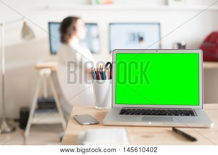 Green screen laptop computer and a glass with color pencils on wooden table, creative office on the background