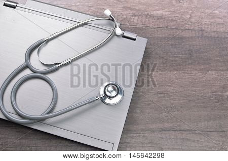Grey stethscope on top of laptop at wooden background