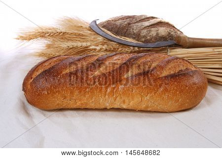 bunch of mown wheat ears with vintage handmade reaper hook sickle and rye and white dark french fresh bread loaf on light linen tablecloth