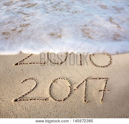 2016 2017 inscription written in the wet beach sand with sea water wave. Inscription 2016 and 2017 on a beach sand, the wave is almost covering the digits 2016.
