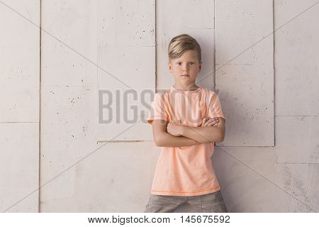 Stylish boy stands against the wall . On the left there is space for text on the wall . Children's fashion