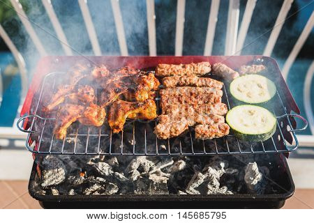 Delicious meat on barbecue grill with coal on balcony. Grilling food on a balcony or a terrace with wonderful view. Small cheap BBQ grill at home.