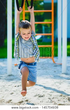 Smiling kid having fun at playground. Child doing gymnastic exercises.
