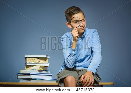 school concept. doubt boy sitting on desk and looking into a magnifying glass.