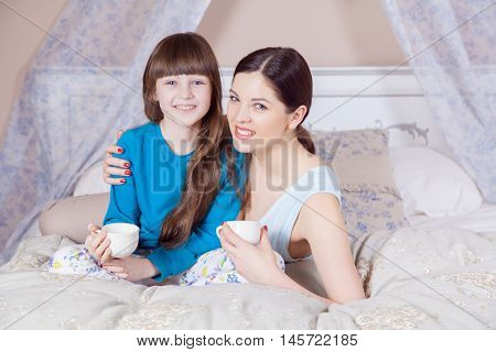 Mother And Daughter Lay In Bed And Drinking Tea.