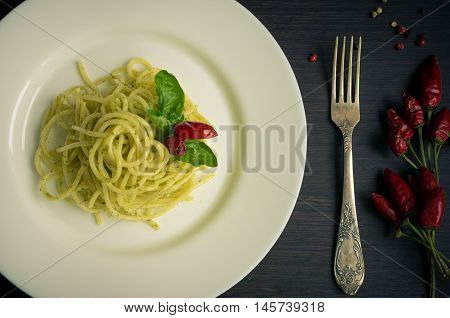 Close up italian pasta spaghetti with homemade green pesto sauce and basil leaf with a fork on dark background. Delicious healthy vegetarian food. Italian food concept. Top view.