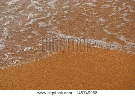 Wave of sea on sandy beach with foam, a lot of space for text top vie