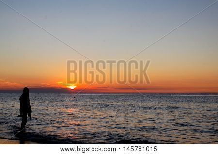 The dark shape of a girl on the background of orange sunset over the sea.