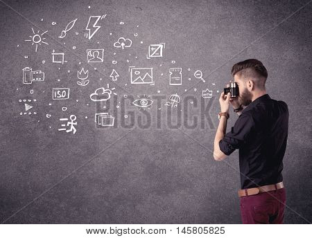 An elegant hipster guy trying to use a vintage camera with camera settings icons drawn on wall, like flash, white balace or ISO value concept