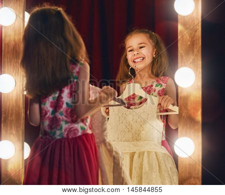 Cute little fashionista. Happy child girl try on outfits looking at mirror.