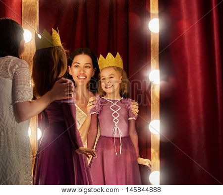 Cute little actress. Young mother and her daughter child girl in Princess costume on the background of theatrical scenes and mirrors.