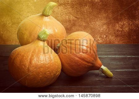 Three pumpkins lying on the wooden desk. Brown light grunge texture background. Edited as a vintage photo.
