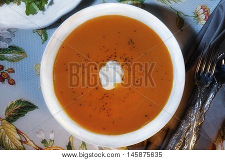 Low key image of carrot ginger tofu puree soup on a floral table cloth with dappled sunlight on the soup.
