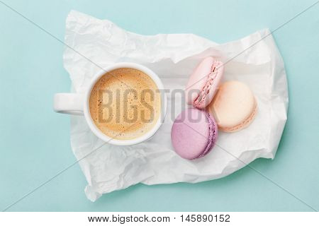 Cup of coffee with macaron on blue background from above, flat lay