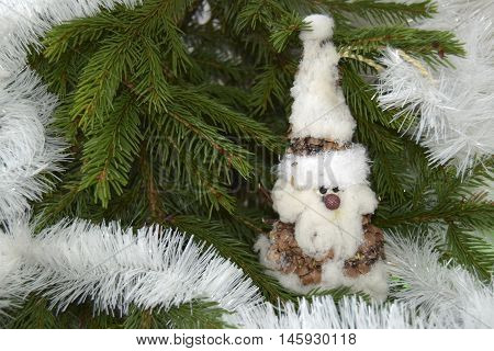 Christmas toy in the form of the gnome. The toy is located on a fir-tree. The gnome is made of fir cones and cotton