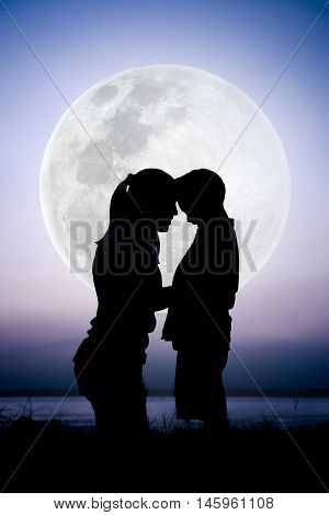 Silhouette side view of mother and child enjoying at riverside. Mother with her son on colorful sky and large moon background. Cool colors tone photo effect. The moon were NOT furnished by NASA.