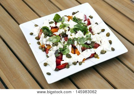 square white plate with caprese salad and capres on wooden table