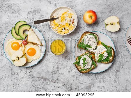Helpful breakfast - fried egg poached eggs avocado apple muesli and orange juice on light surface top view