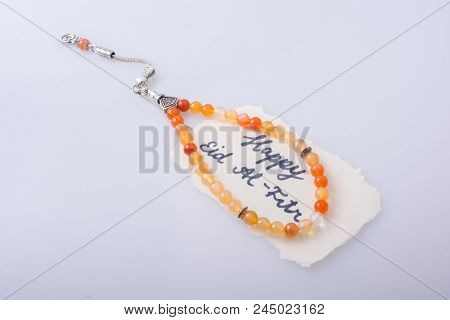 The Word Eid El Fitr  Written On Torn Paper Beside Prying Beads