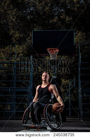 Cripple Basketball Player In A Wheelchair Holds A Ball On Open Gaming Ground.