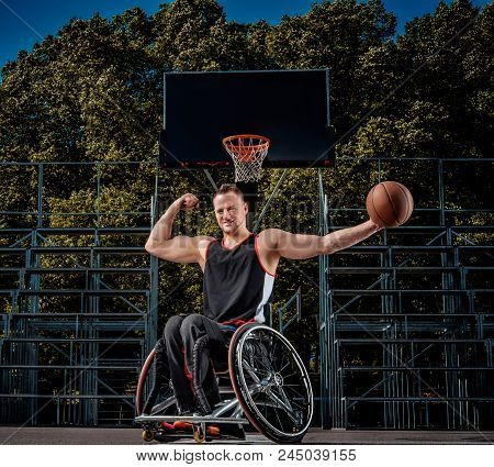 Happy Basketball Player In A Wheelchair Pose With A Ball On Open Gaming Ground.