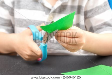 Cutting Out Of Colored Paper. A Child With An End-point Scissors Cuts Green Paper. The Concept Of Ch