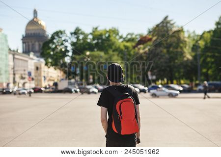 Back View Of Young Stylish Man Tourist Walking At Palace Square Near Saint Isaac's Cathedral In Sain