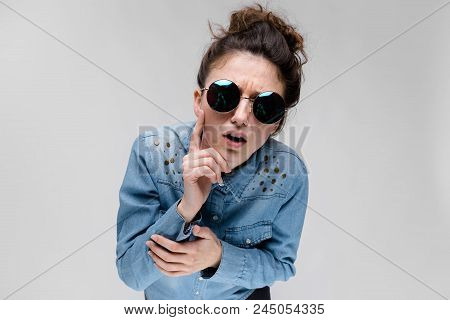 Young Girl In Round Glasses On A Gray Background. Portrait Of A Young Beautiful Girl. Charming Girl 